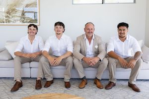 Family portrait, groomsmen in white shirts and khaki pants sit casually together on a white sofa