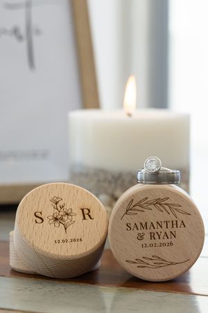 Personalized wooden ring boxes with engraved names and a lit white candle in the background.