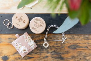 Wedding rings rest on rustic wooden surface beside floral gift box and decorative elements. wedding details