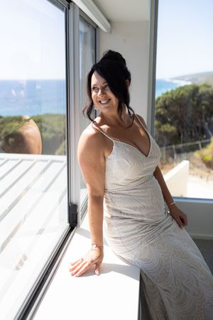 A person in a white beaded wedding dress poses near a window in natural light.