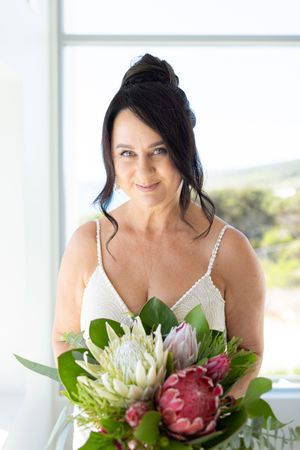 A bride in white holds a stunning bouquet featuring pink and white protea flowers
