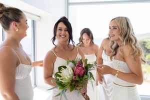 Candid moment of wedding party in white dresses with native flower bouquet.