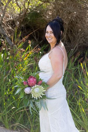 A bride in a white lace dress poses against a coastal backdrop Yallingup