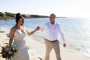A couple shares a playful moment while walking along a beautiful beach on their wedding day.