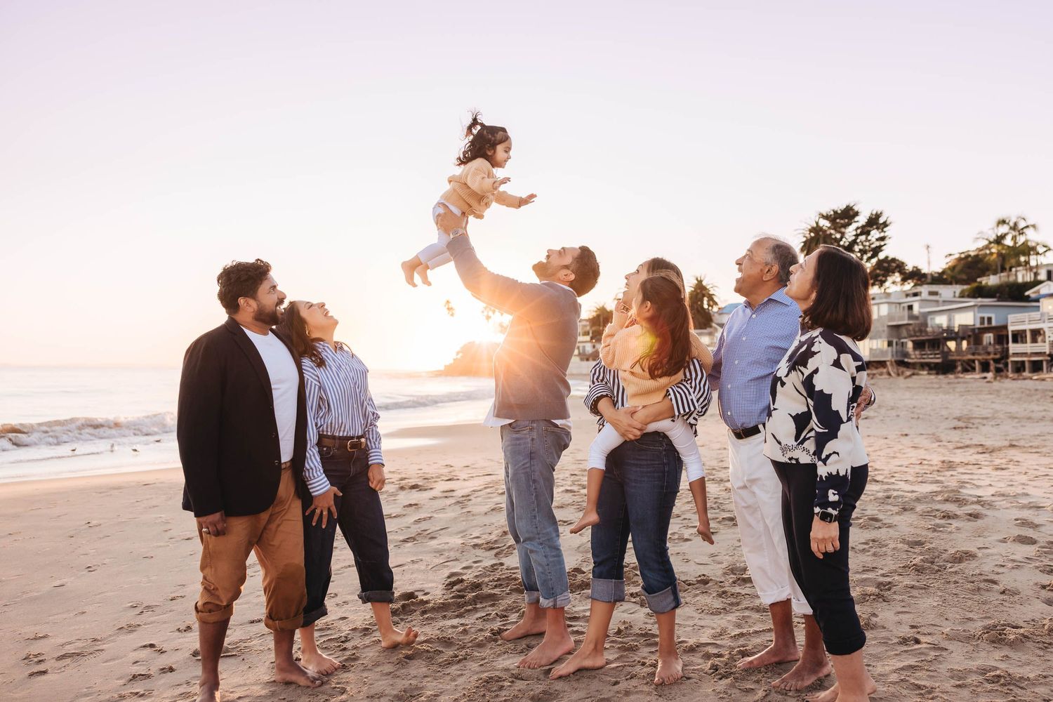 A group of people enjoy a playful moment together on a beach at sunset with warm golden lighting.