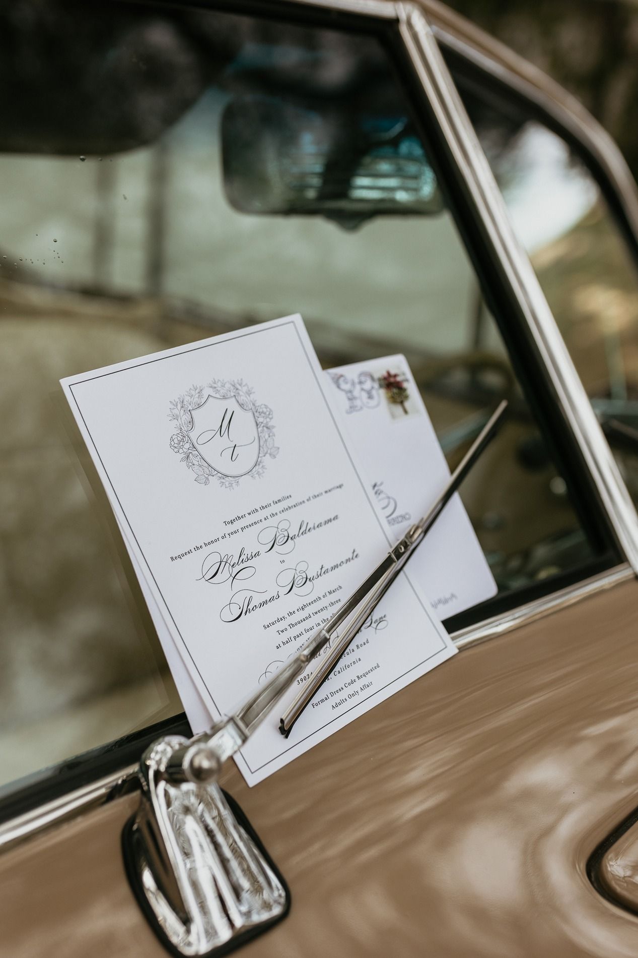 Elegant white wedding invitation with monogram rests on classic car window at The Oaks at Duncan Lane.
