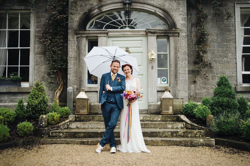 A romantic wedding couple poses in front of a historic stone mansion with elegant architectural details.