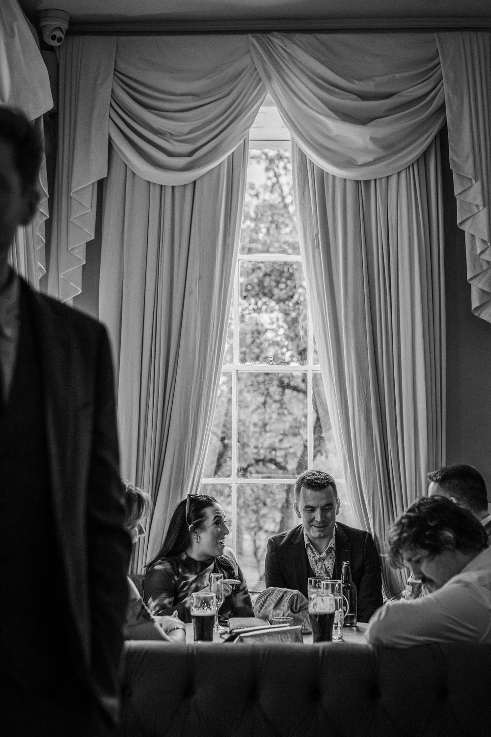 A series of black and white photographs showing people dining at an elegant table with draped curtains in the background.