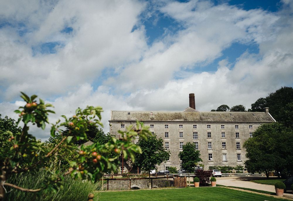 Large historic stone building with multiple stories set against a blue summer sky with white clouds.