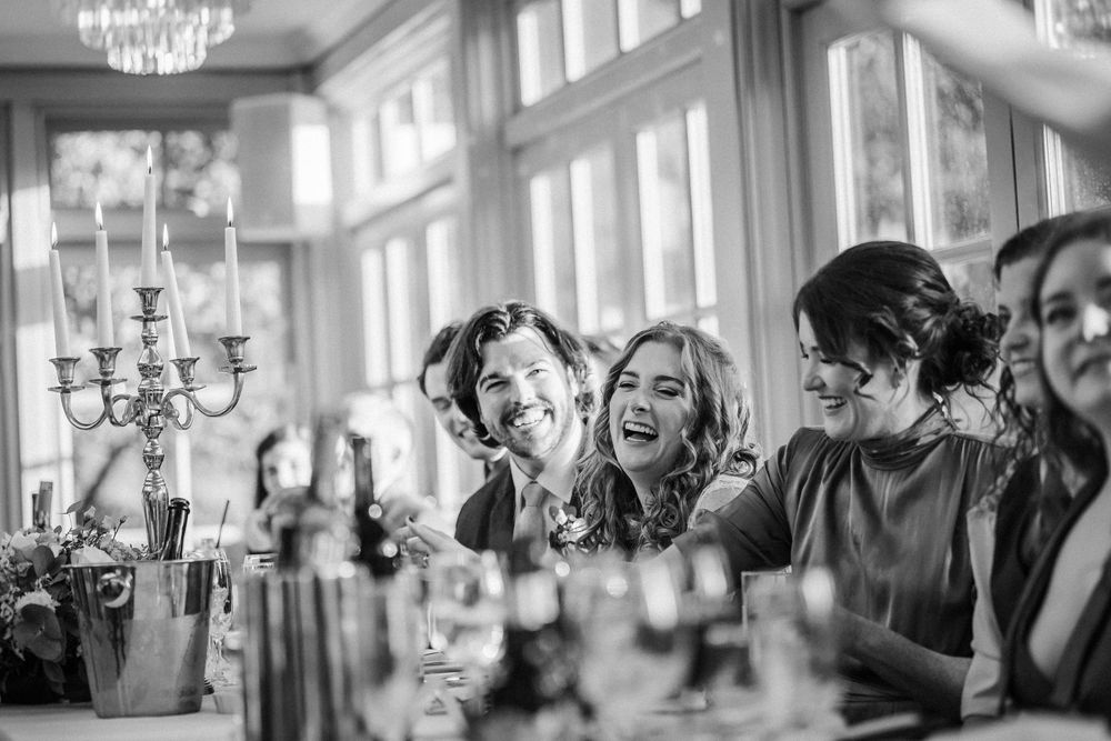 Black and white candid photograph of people laughing together at an elegant dinner party with chandeliers.