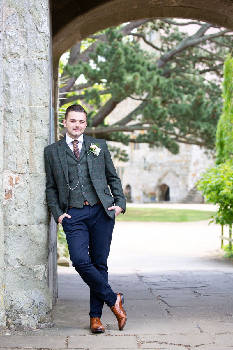 Groom leans in handsome pose of medieval priory | Michelham Priory