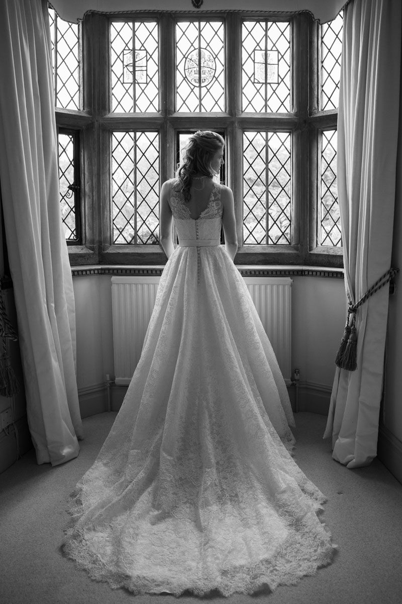Full length shot of bride with dress and long train, standing in large and grand window of historic house