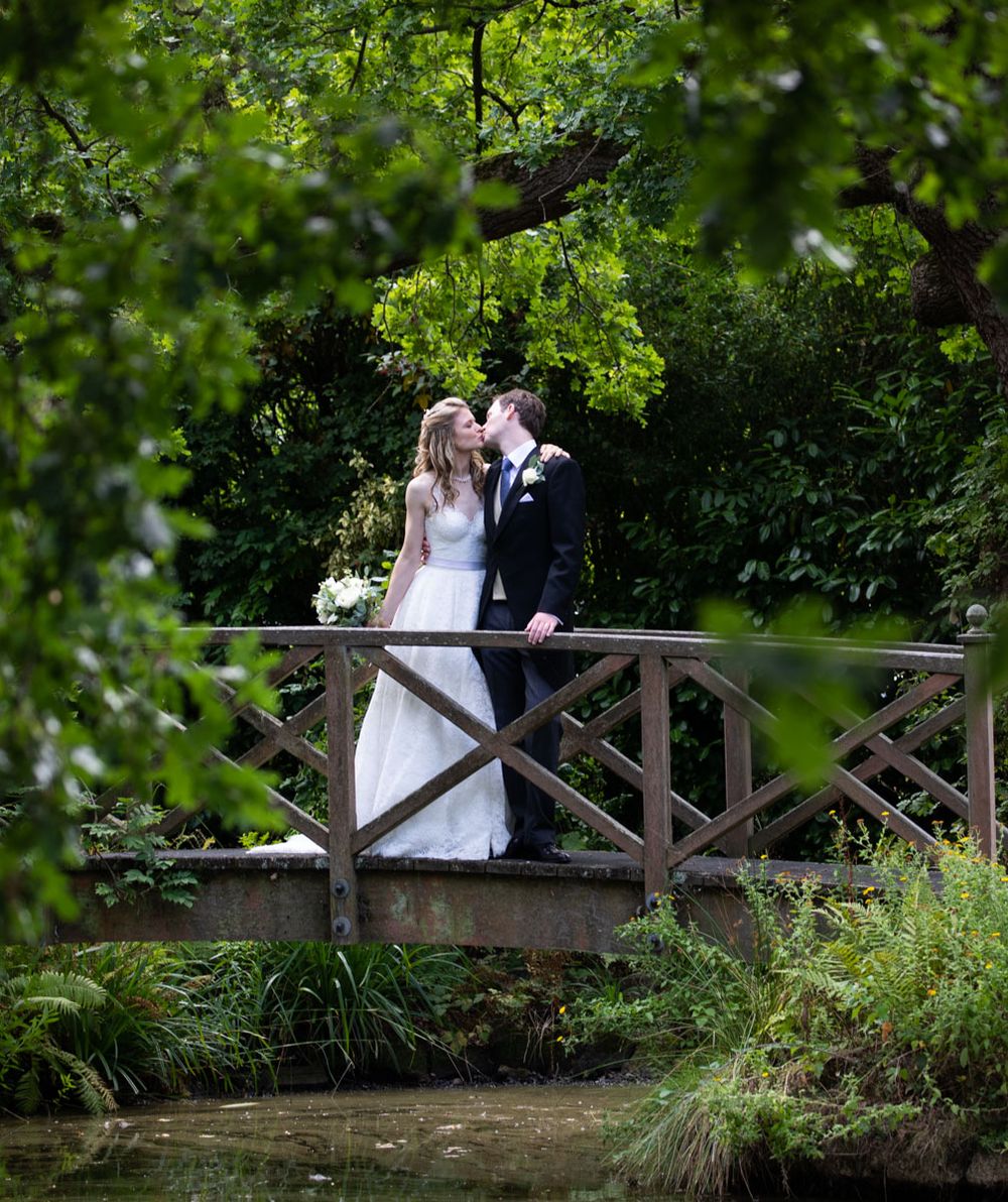Bride and groom share a kiss on bridge in stunning country house garden