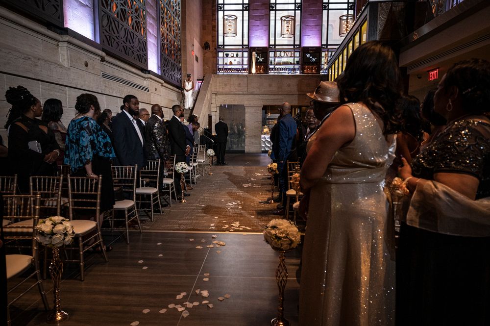 Wedding guests watch a couple's first dance in a dimly lit ballroom with warm ambient lighting.