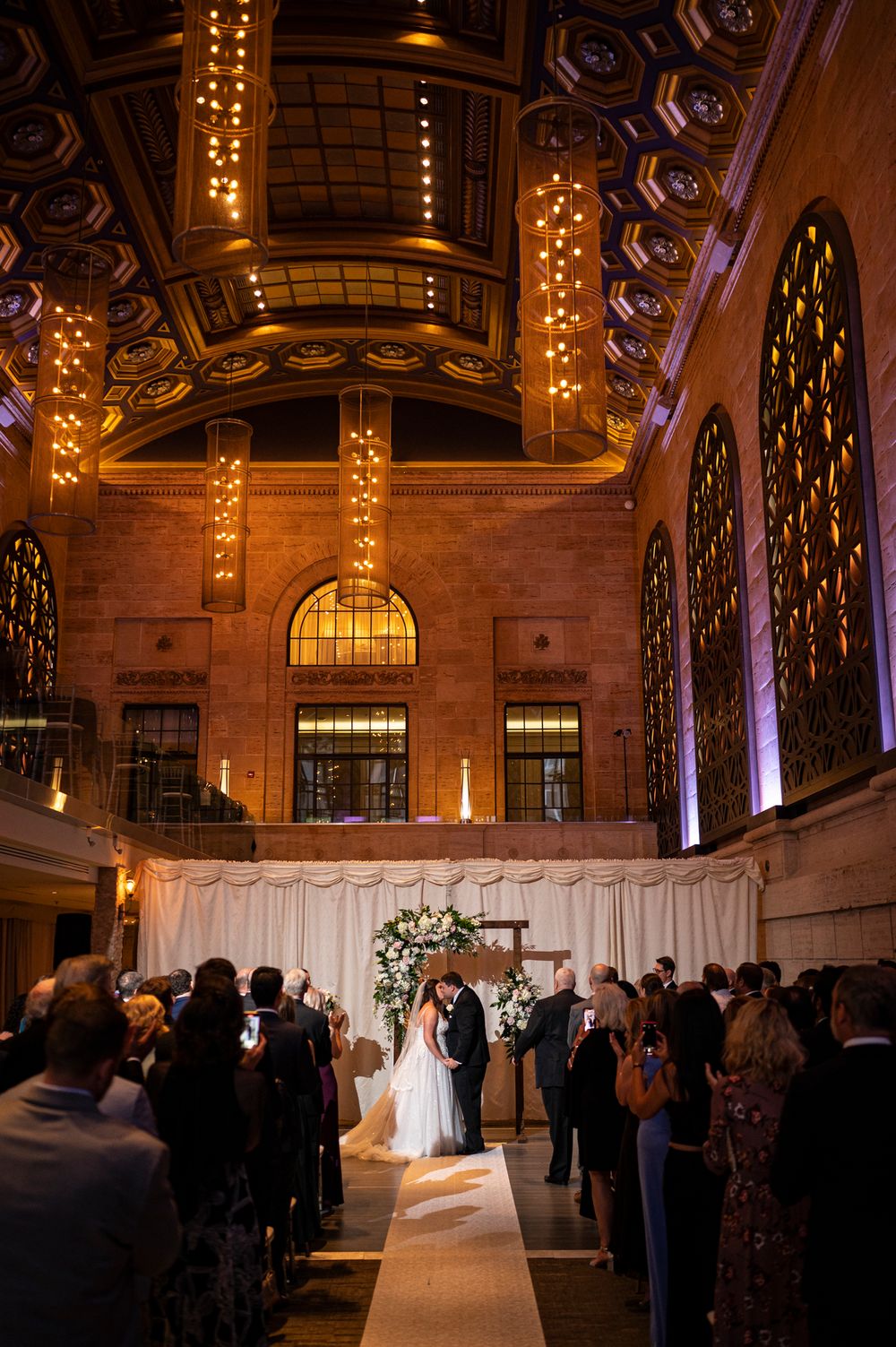 Wedding ceremony in an ornate historic venue with vaulted ceilings and warm lighting creates an elegant atmosphere.