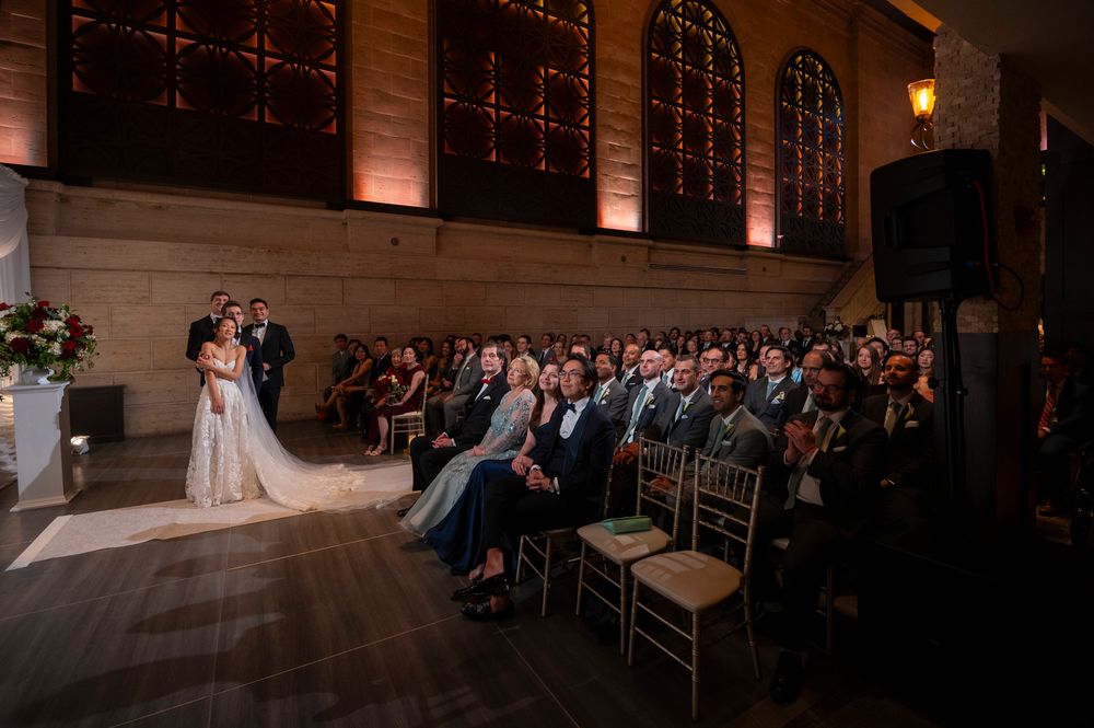 Wedding ceremony at Union Trust in Philadelphia showing guests looking up at a screen during a couples ceremony.