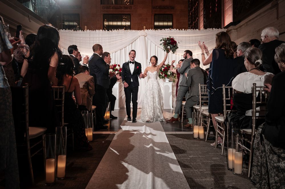 A couple walks down the aisle during their wedding ceremony in a rustic brick venue with dramatic lighting and candles.