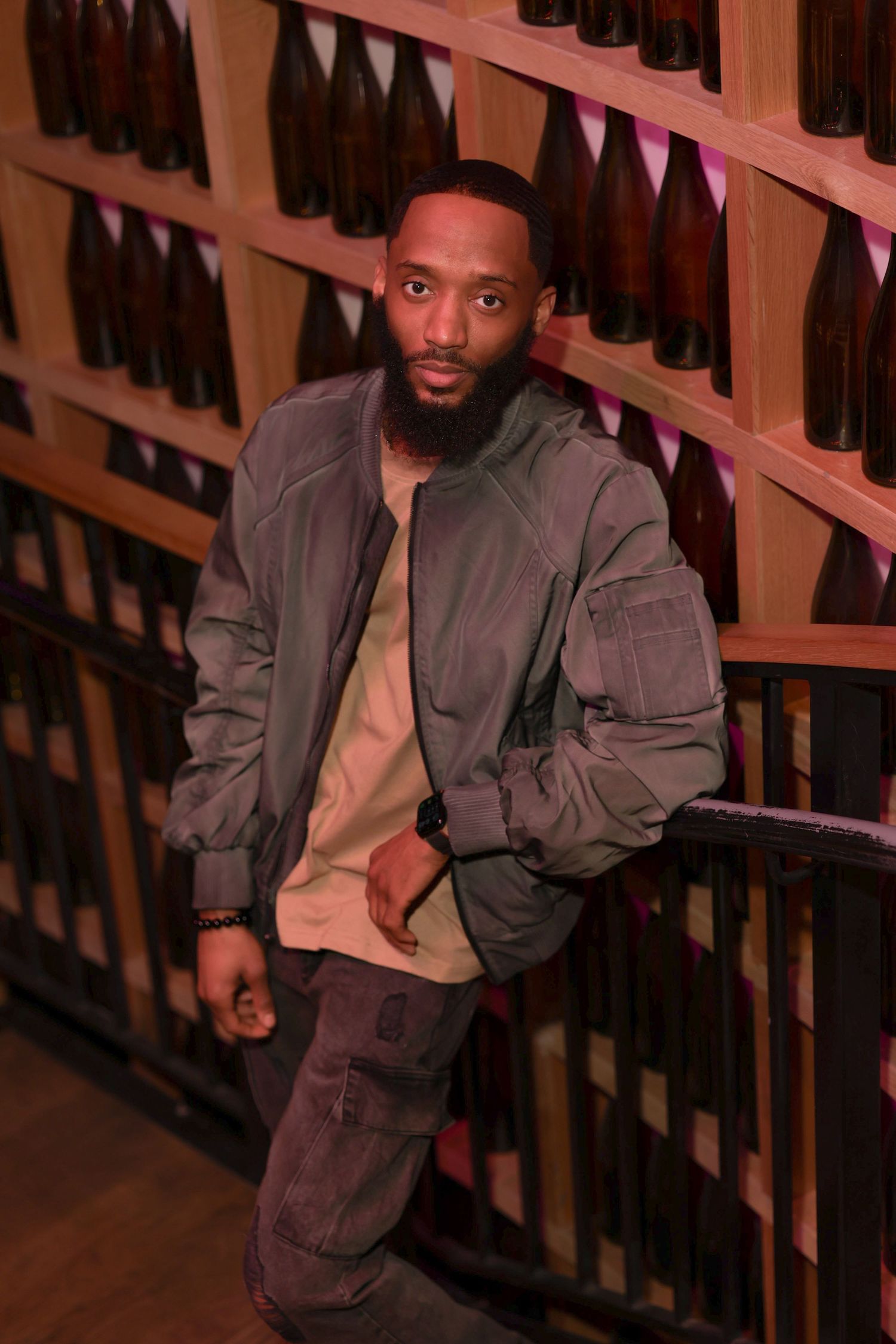 A person in a dark jacket sits on wooden stairs in a dimly lit setting with a warm reddish glow.
