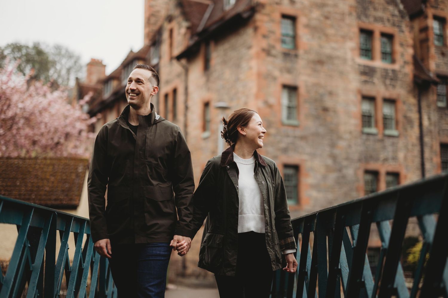 A couple walks together and laughs while strolling past historic brick buildings on a spring day.