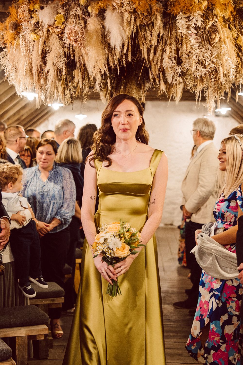 Wedding guests gather in an elegant venue with hanging floral decor and warm lighting during an evening celebration.