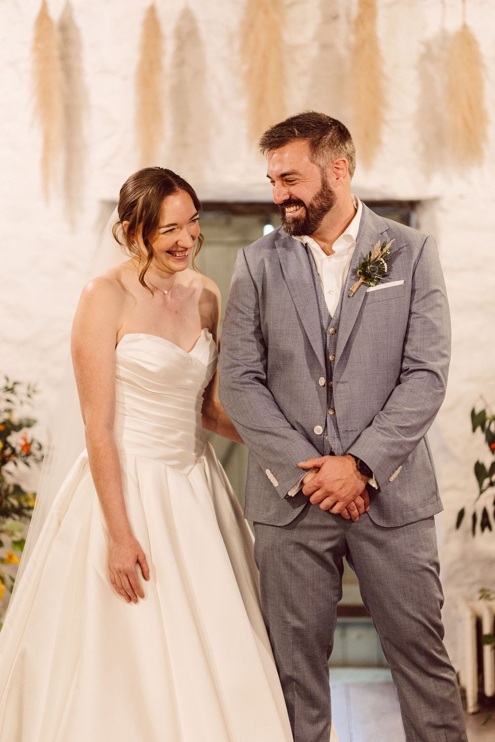 A happy couple shares candid laughing moments in their wedding attire with the bride in white and groom in gray.