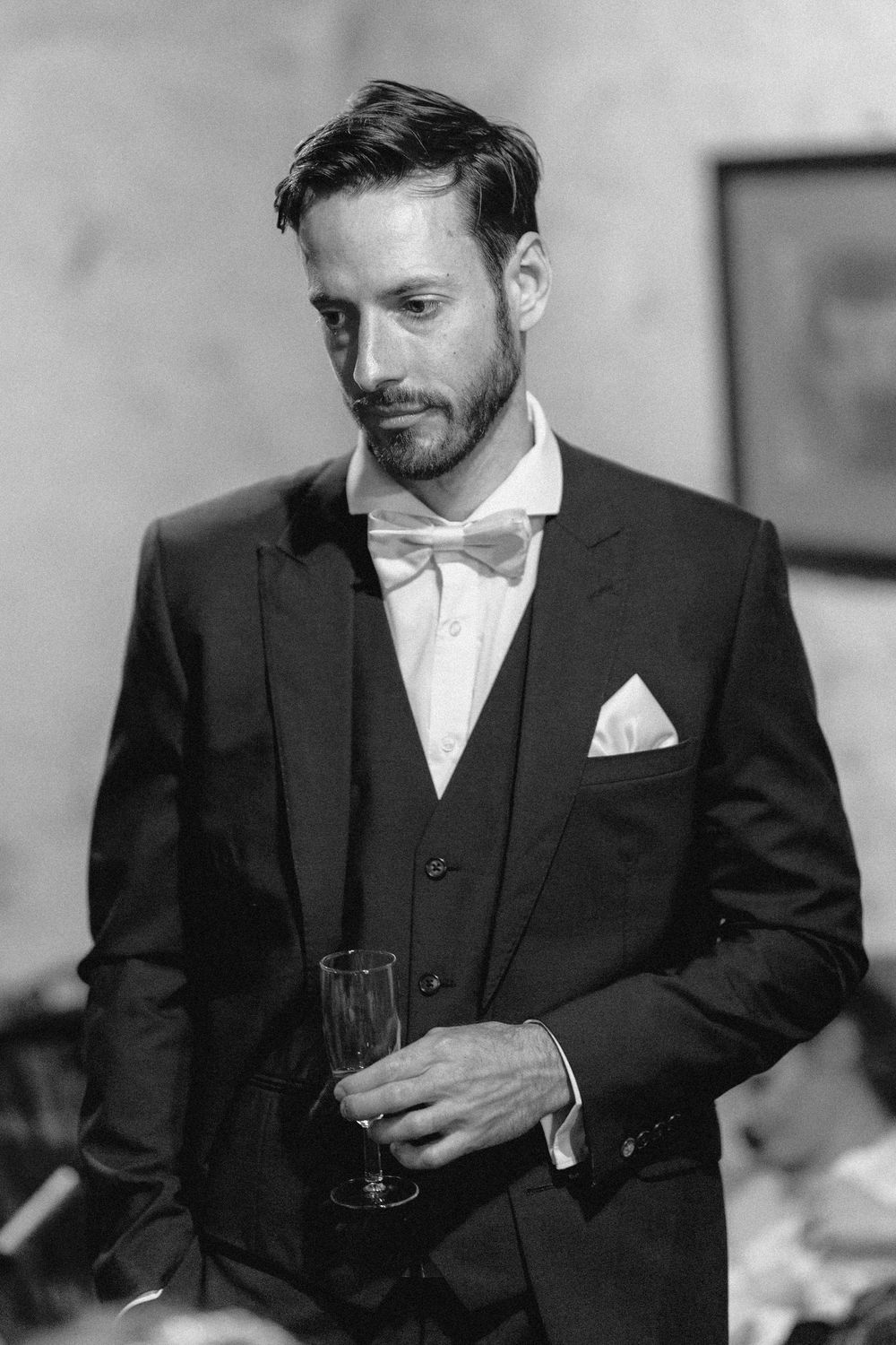 A person in a black suit and white tie sits thoughtfully in black and white photography.