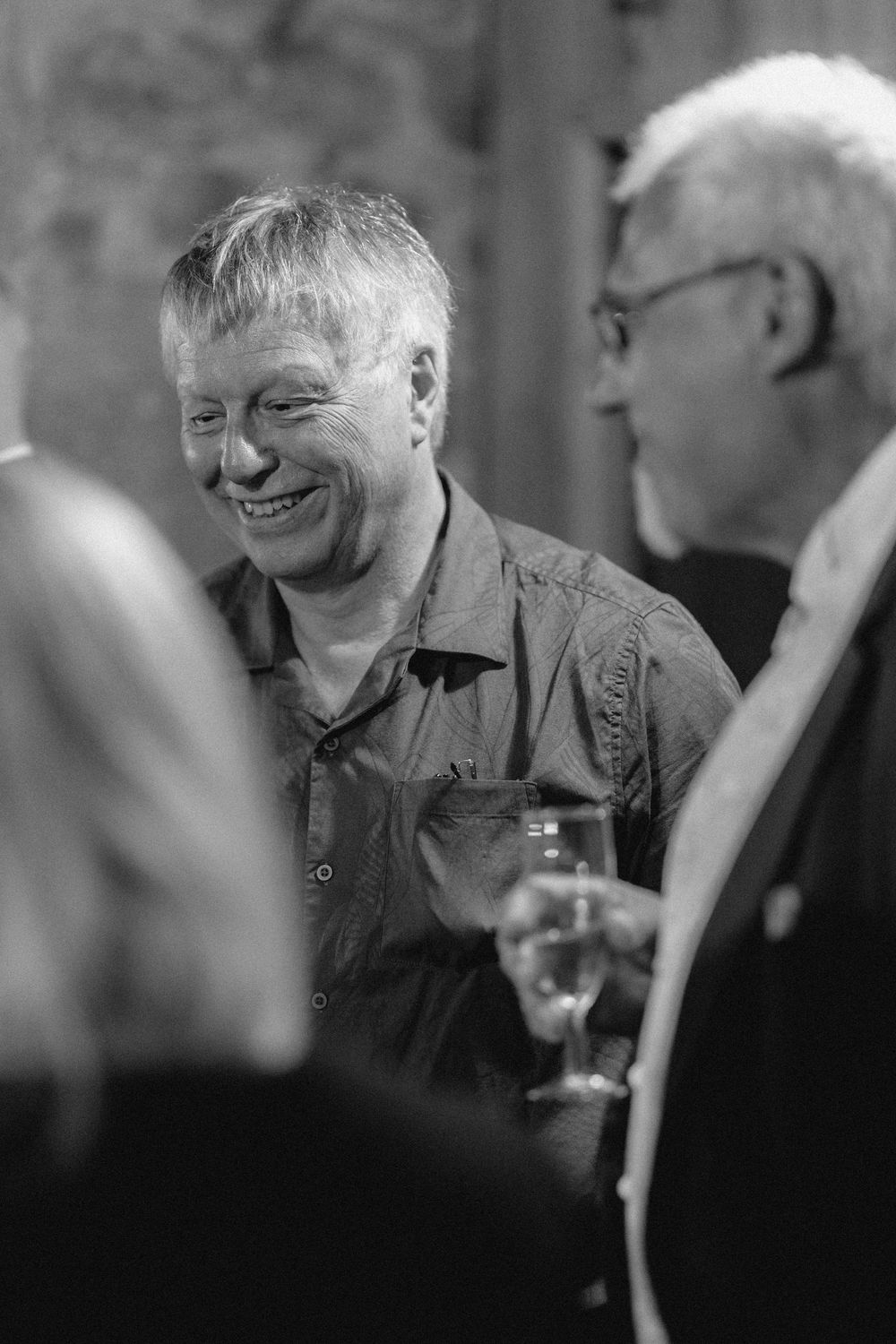 Black and white image sequence showing people laughing and conversing over wine glasses in a dimly lit setting.