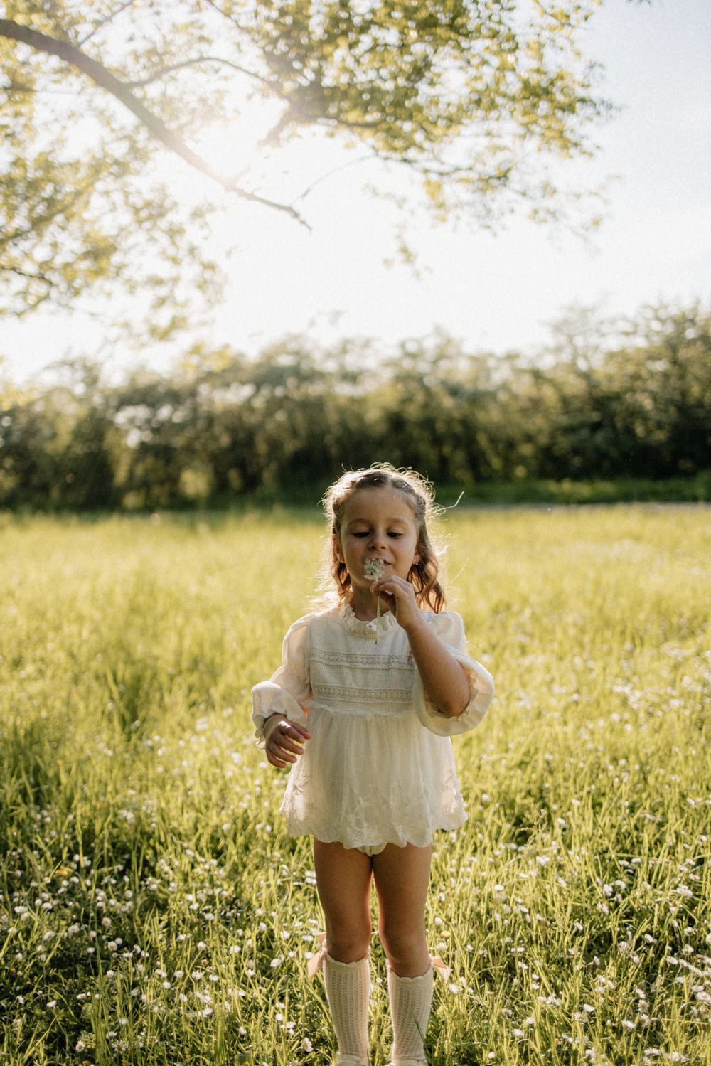 A small child in a white dress plays in a sunny meadow filled with wildflowers during golden hour.
