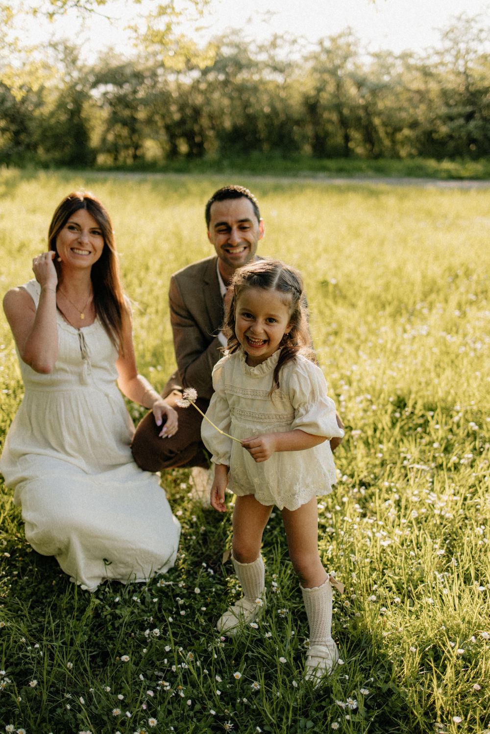 A family sitting together in a sunny wildflower meadow wearing white outfits and sharing joyful moments together.