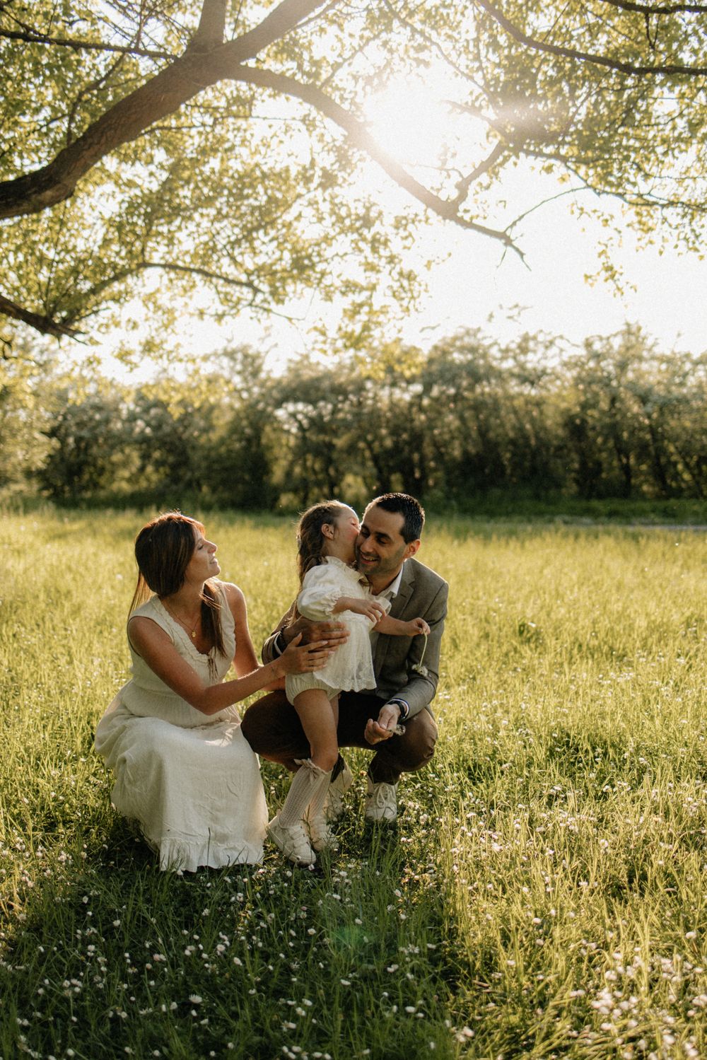 A family shares a tender moment together in a sunlit meadow filled with wildflowers during golden hour.