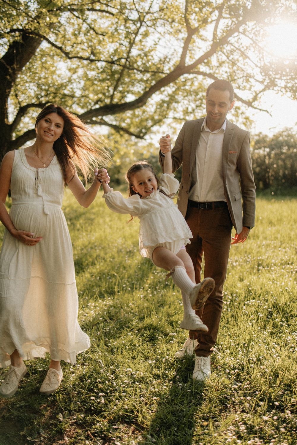 A family plays and dances together in a golden meadow at sunset, creating joyful candid moments.