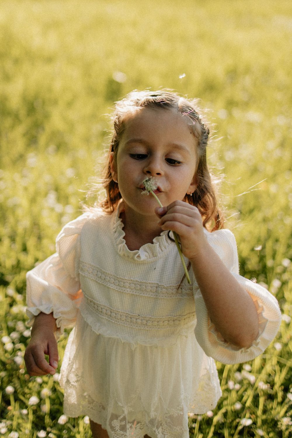 A child in a white dress plays in a sunny field of wildflowers during golden hour.