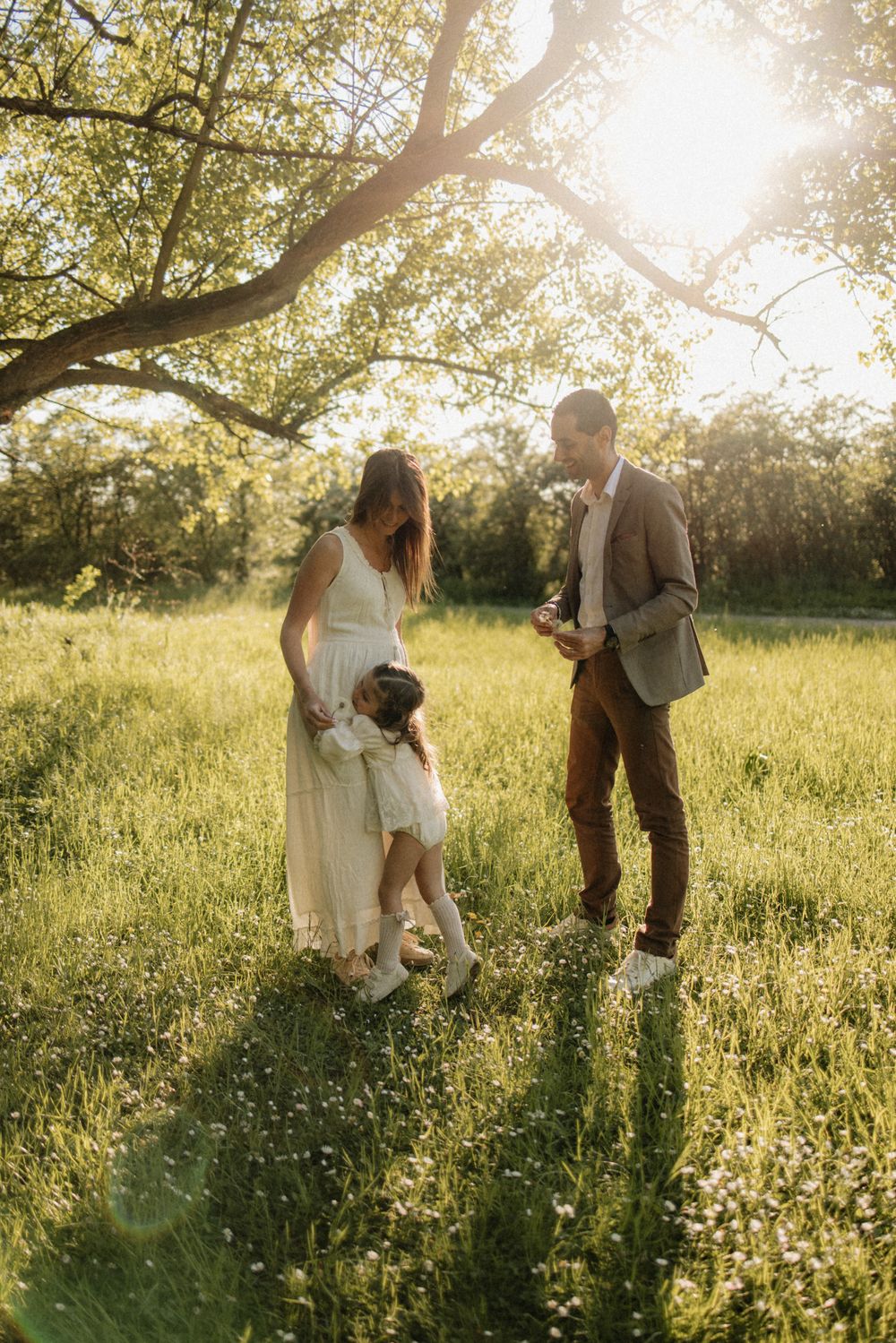 A couple and their dog share a tender moment in a sunlit meadow filled with wildflowers during golden hour.