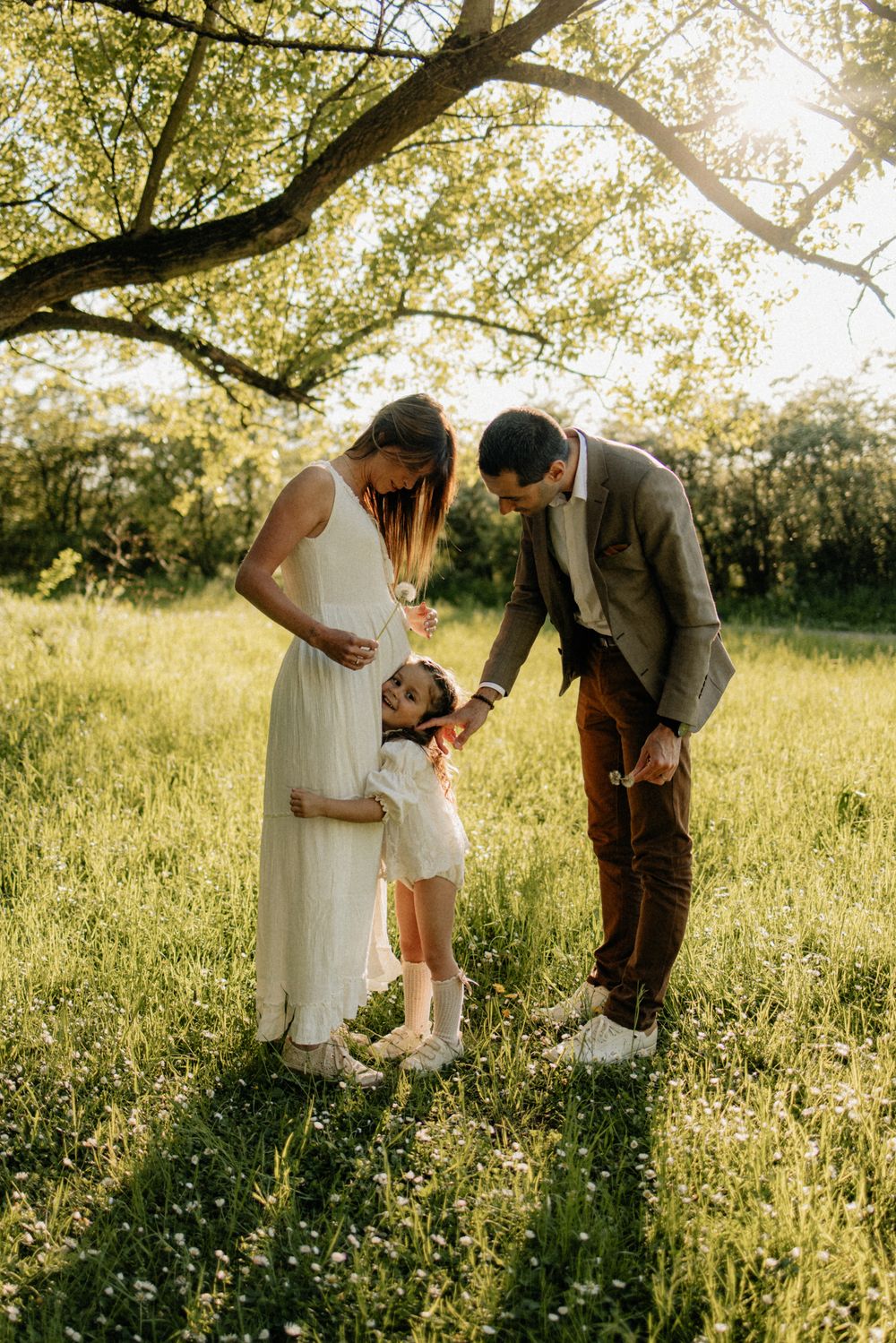 A family shares tender moments together in a sunlit meadow with tall grass and wildflowers during golden hour.