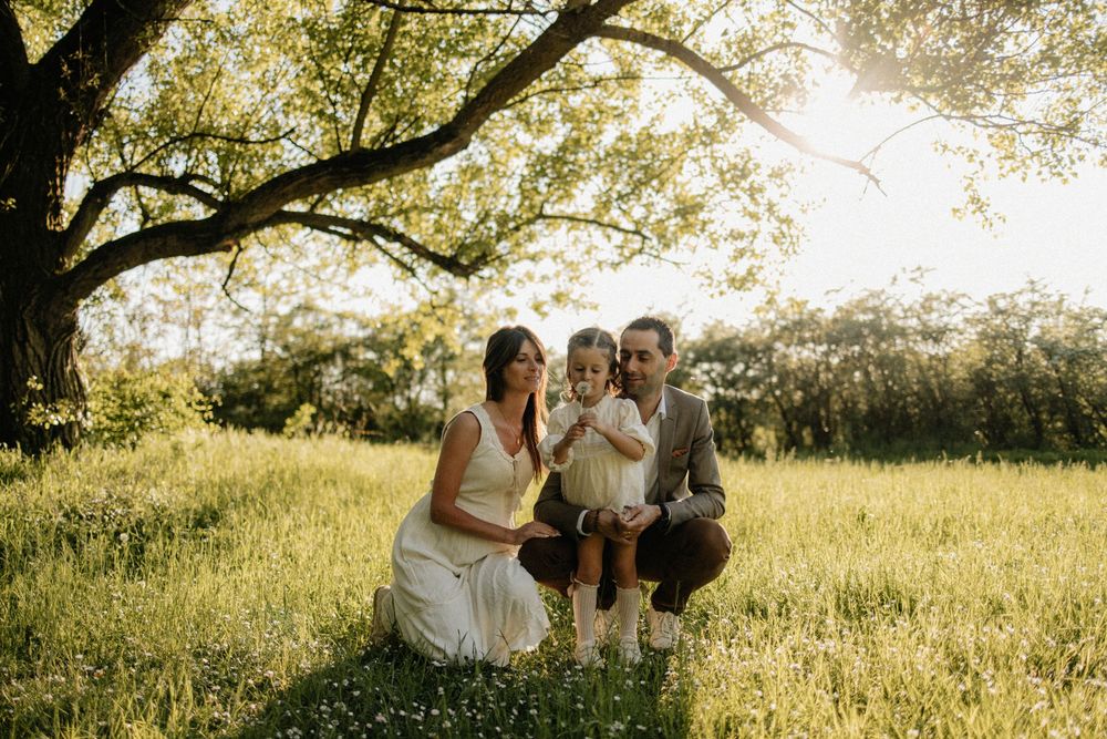 A family sits together in a sunlit meadow under a large tree during golden hour.