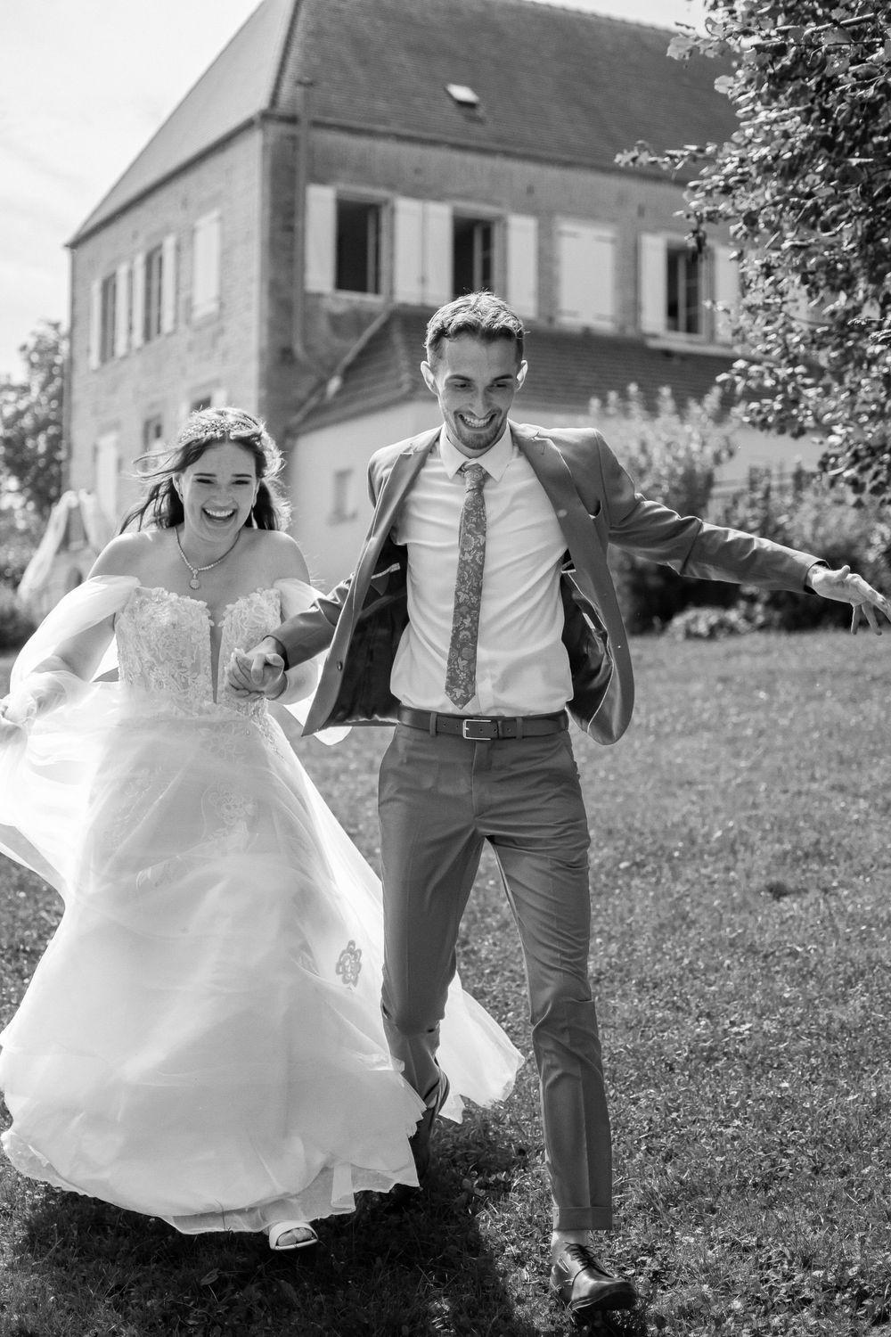 A bride in a white ballgown and groom in military uniform stand in an ornate stone archway as confetti falls around them.