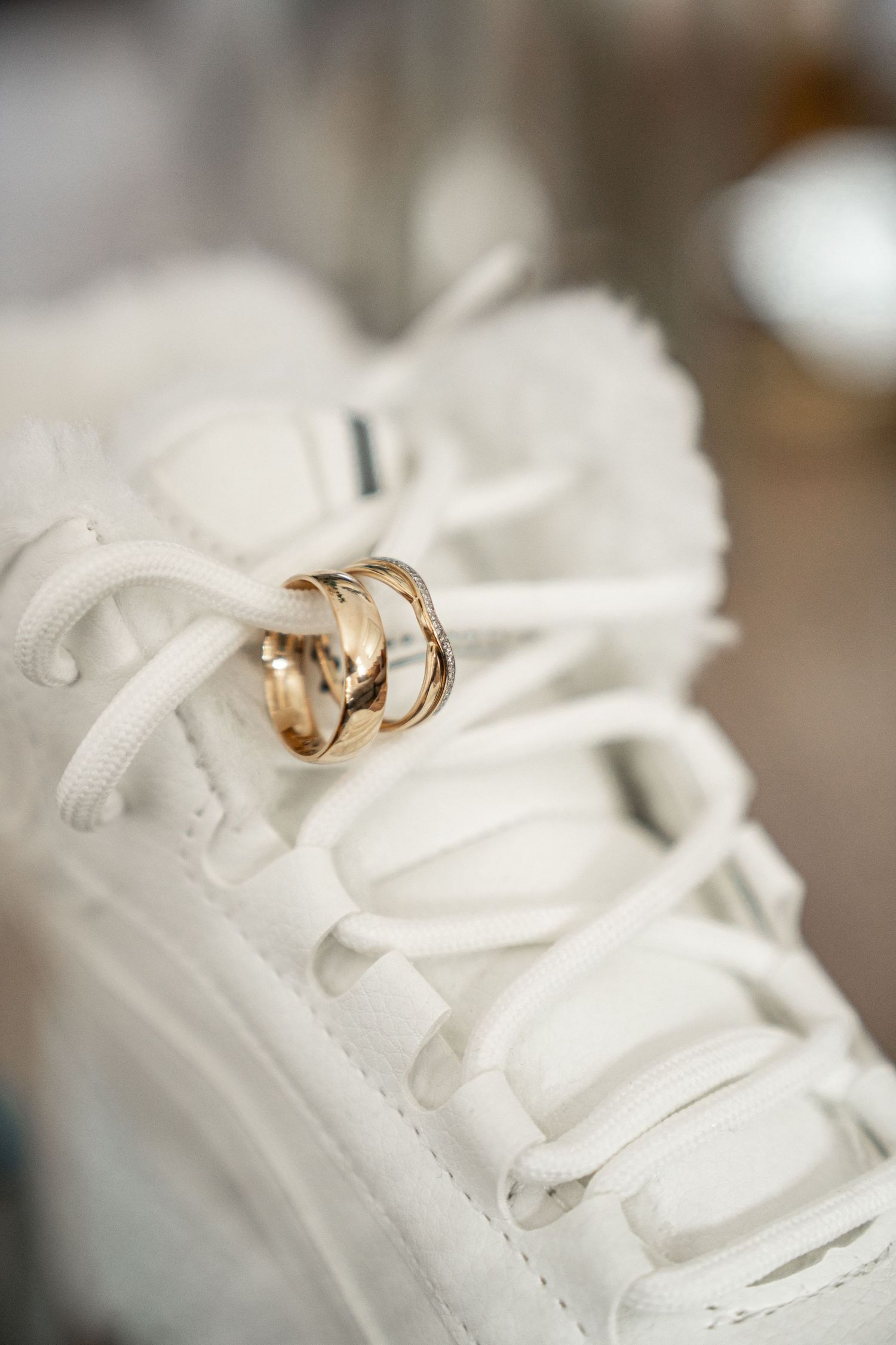 Gold wedding rings balanced on white sneaker laces in artistic wedding detail photography.
