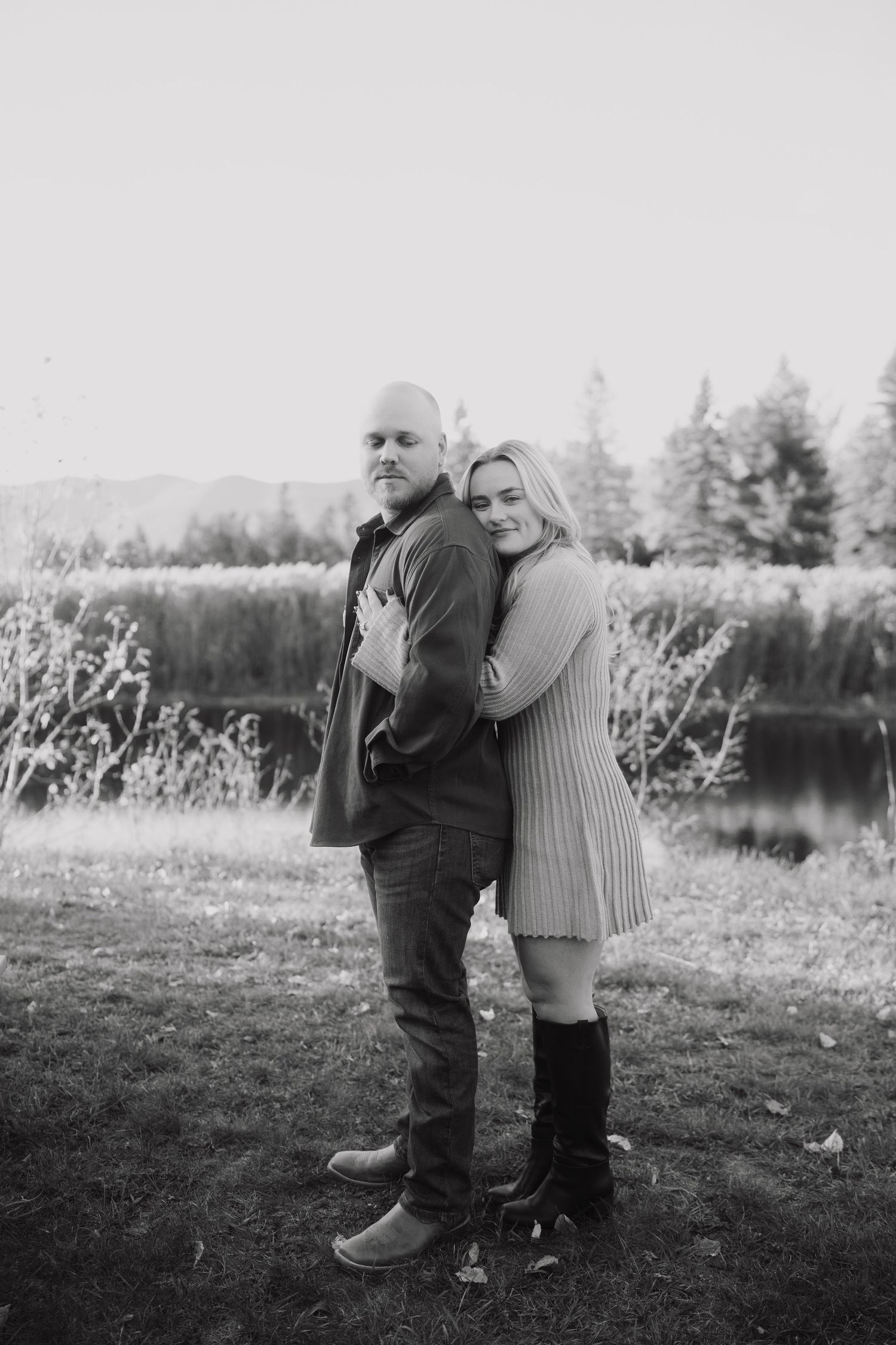 A couple embraces tenderly in a black and white photo taken in a natural outdoor setting with trees in the background.