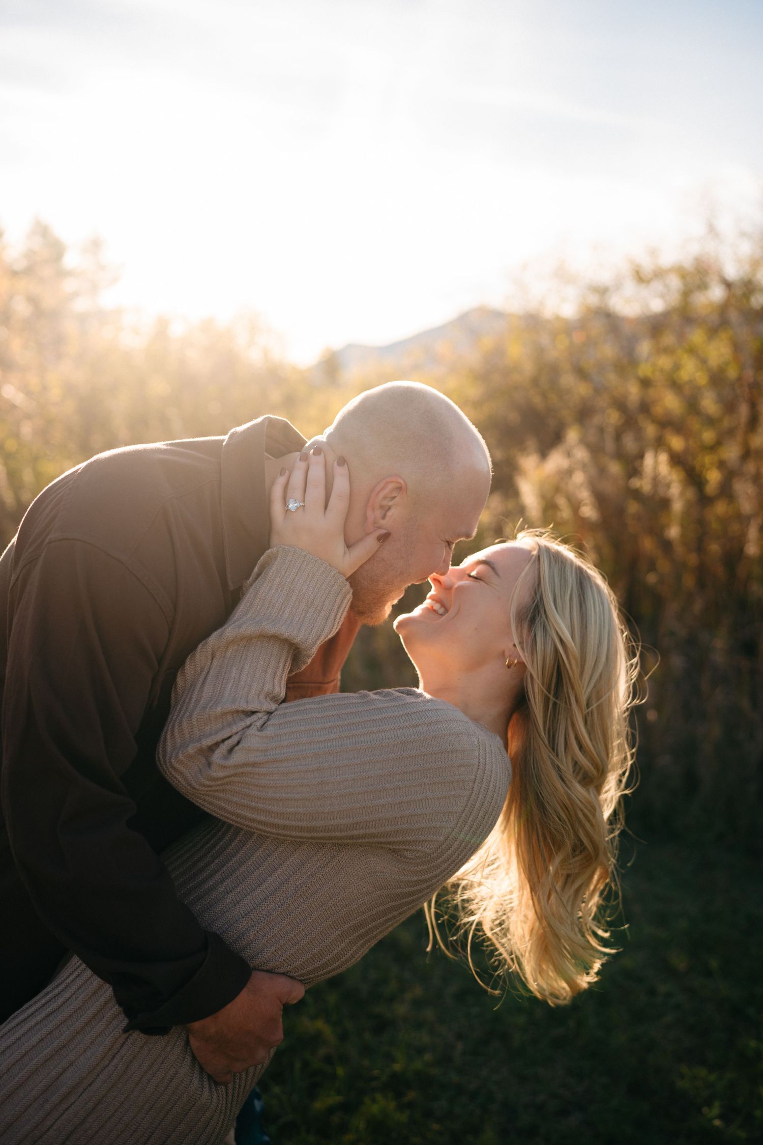 A romantic sunset engagement photo shows a couple embracing and laughing together in golden light.