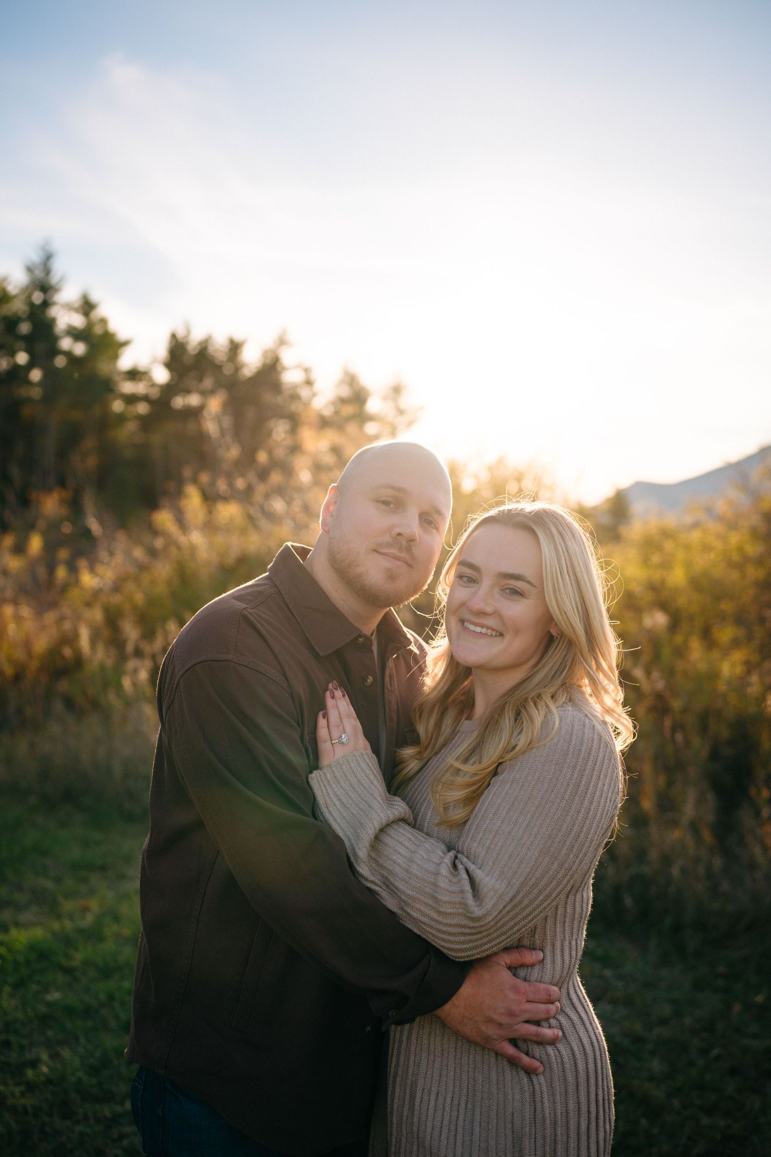 A couple shares a romantic embrace in a golden-lit outdoor setting during sunset.