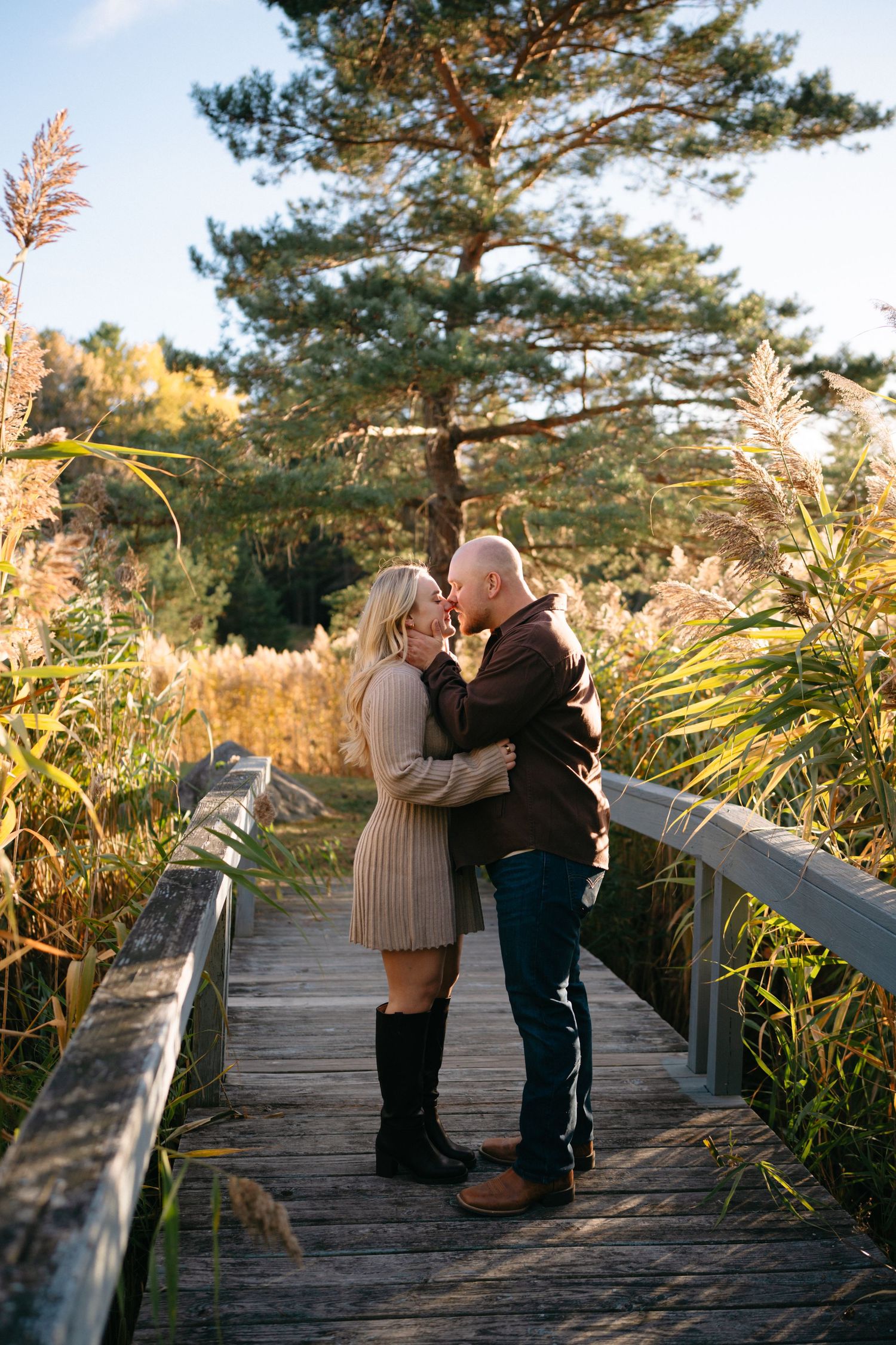 Romantic sunset engagement photos on a wooden boardwalk surrounded by autumn foliage.