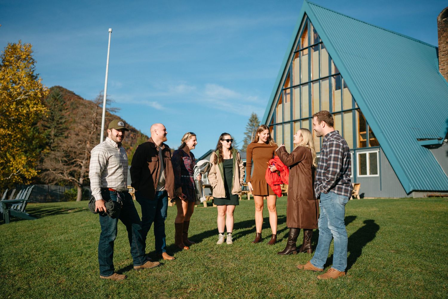 Family members gather for photos on a grassy hill in front of a blue A-frame building on a sunny autumn day.