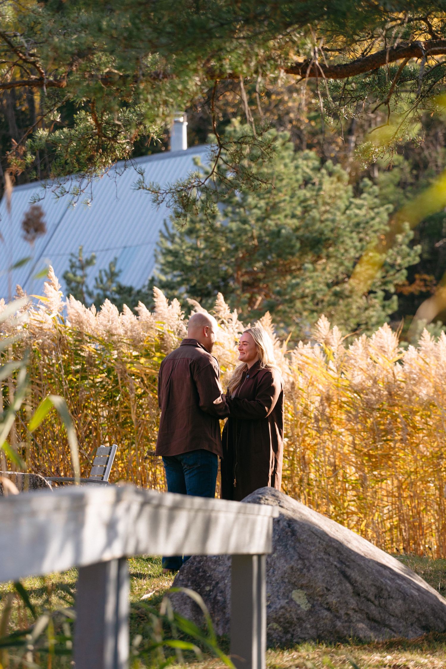 Couple walking together on a path surrounded by golden autumn foliage and tall grasses in warm sunlight.