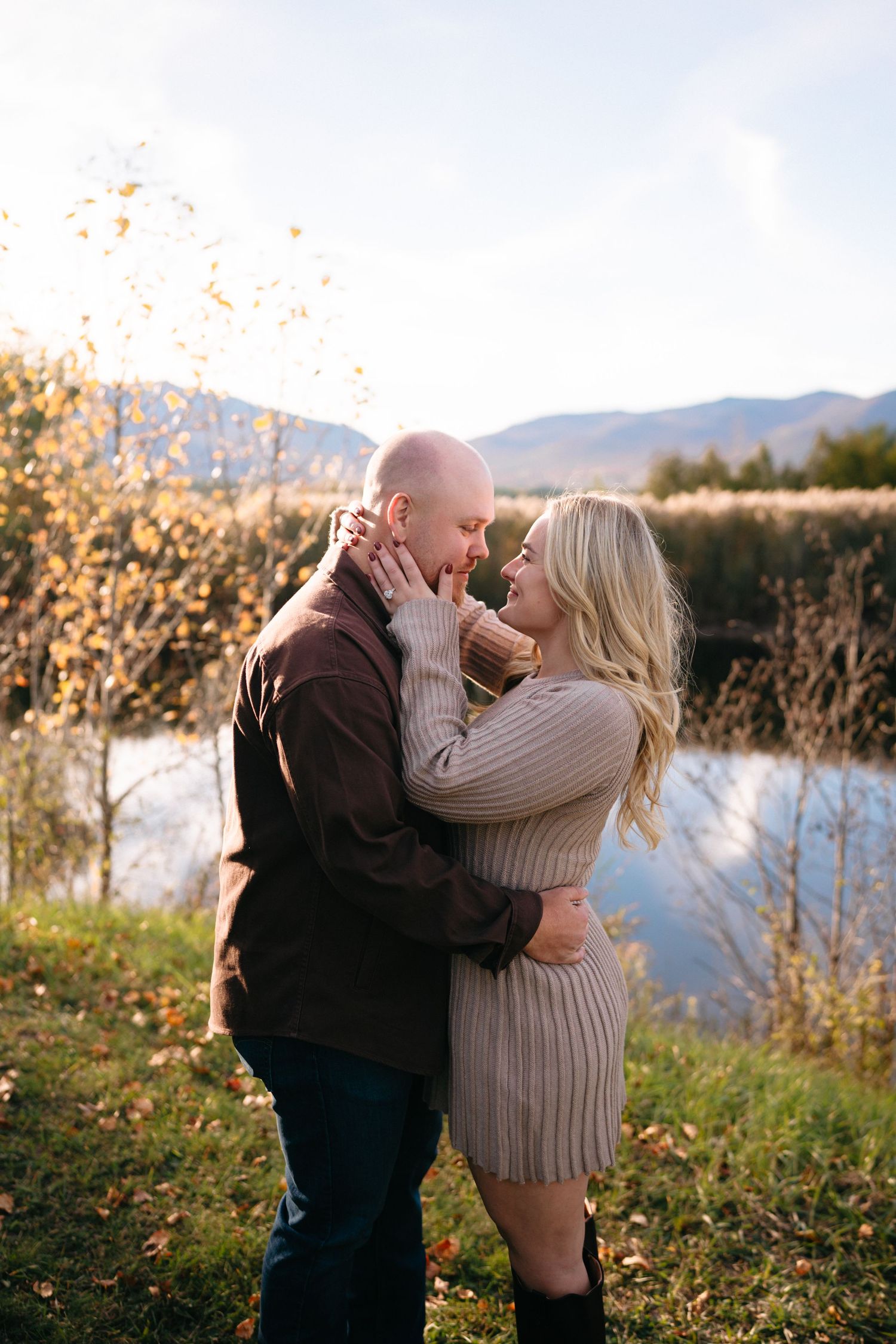 A couple shares a romantic moment in nature with mountains and autumn foliage in the background.