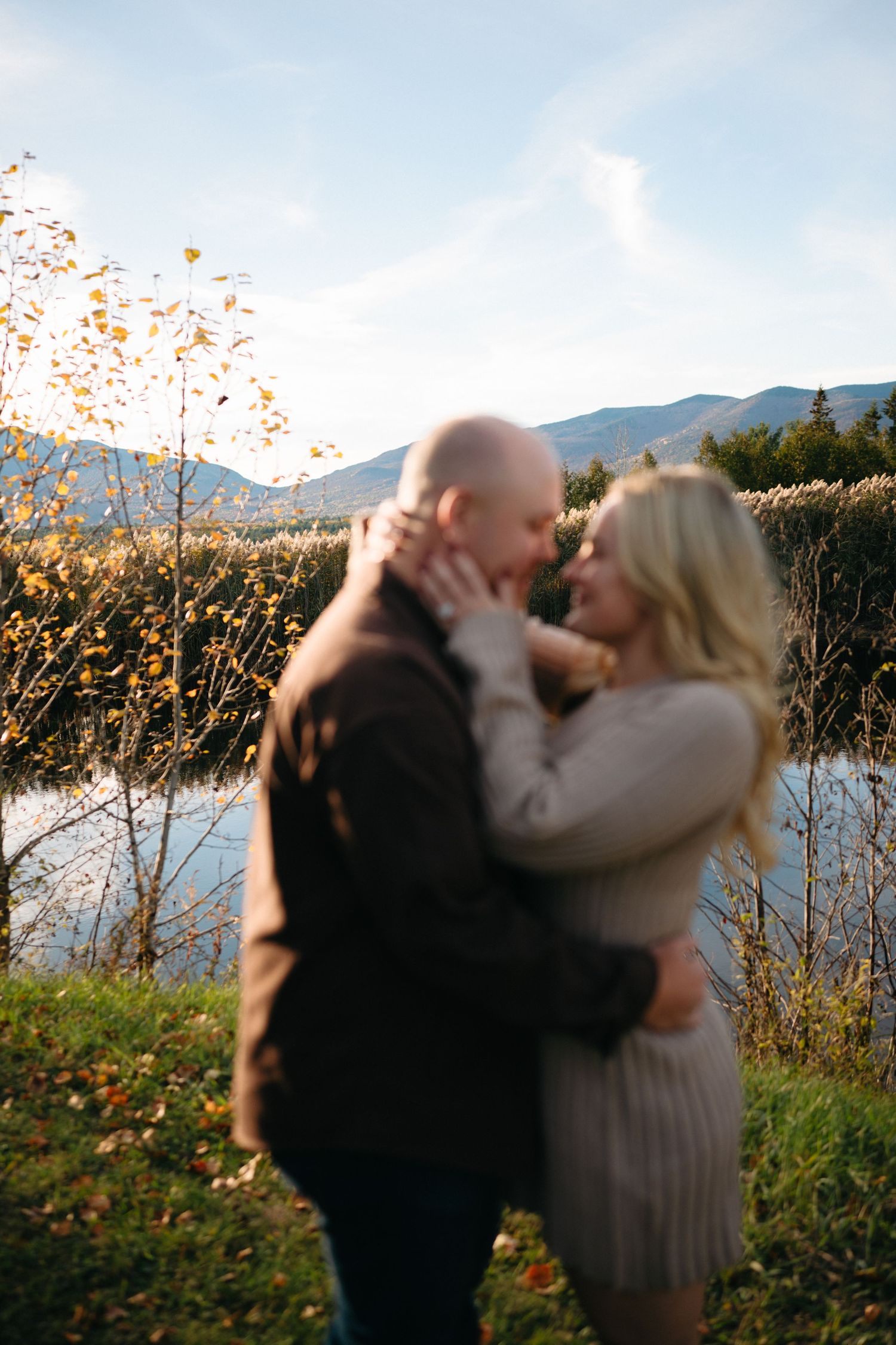 A romantic couple embraces in a series of photos against a scenic mountain landscape with wildflowers at sunset.