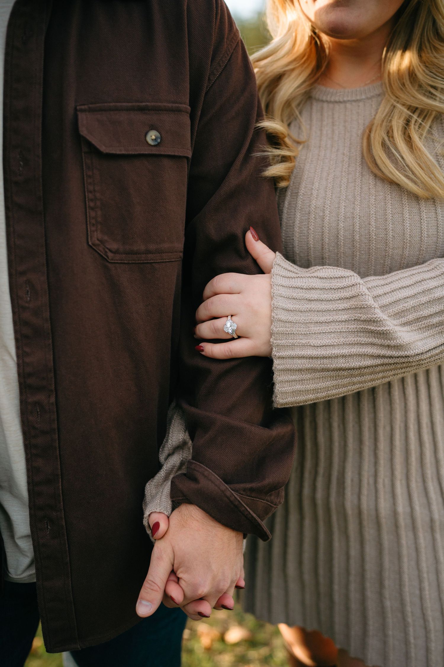 Close-up fashion detail of hands holding while wearing contrasting brown jacket and beige knit sweater.