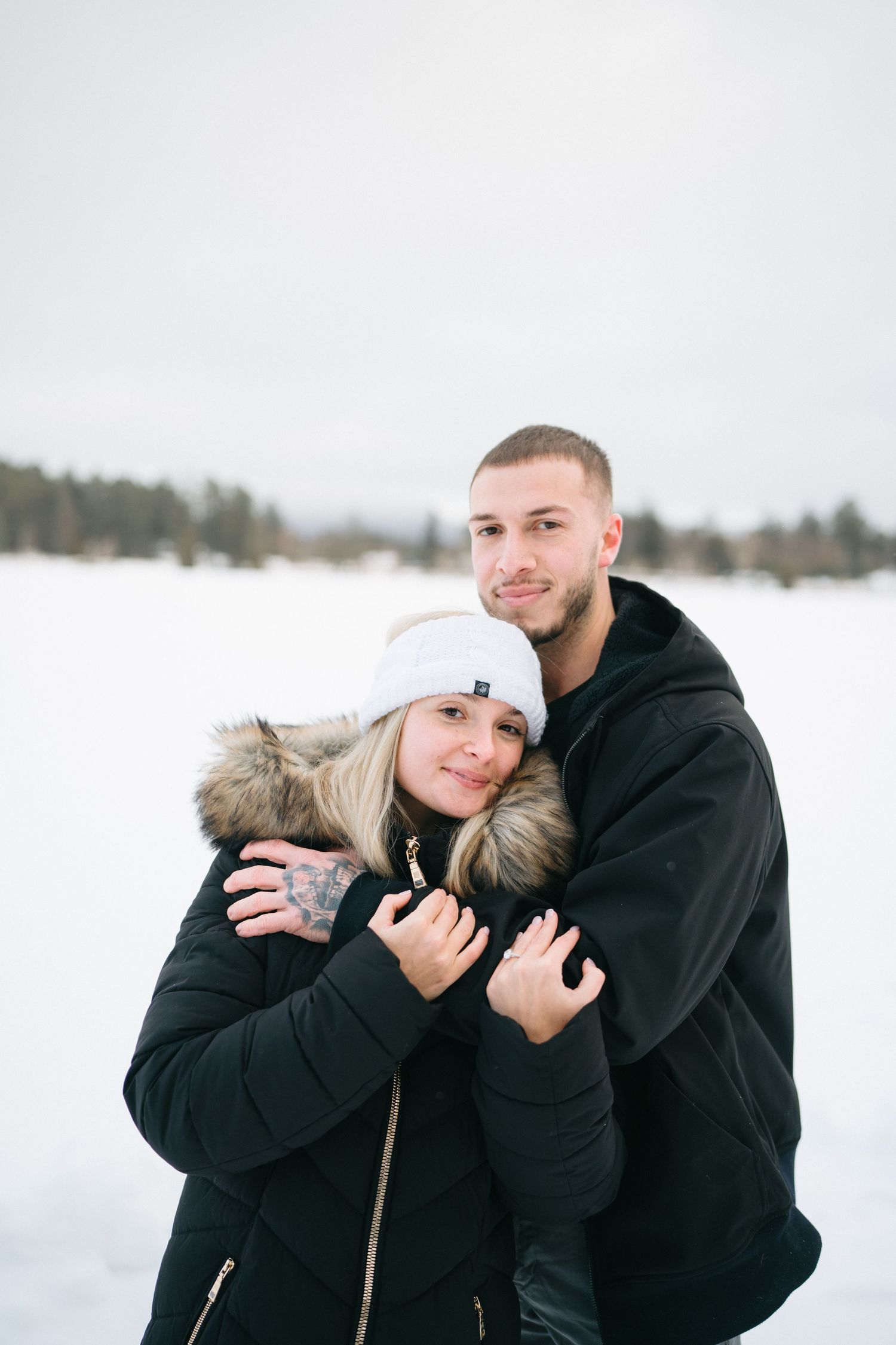 A couple shares intimate winter moments in a snowy landscape wearing black coats and winter accessories.