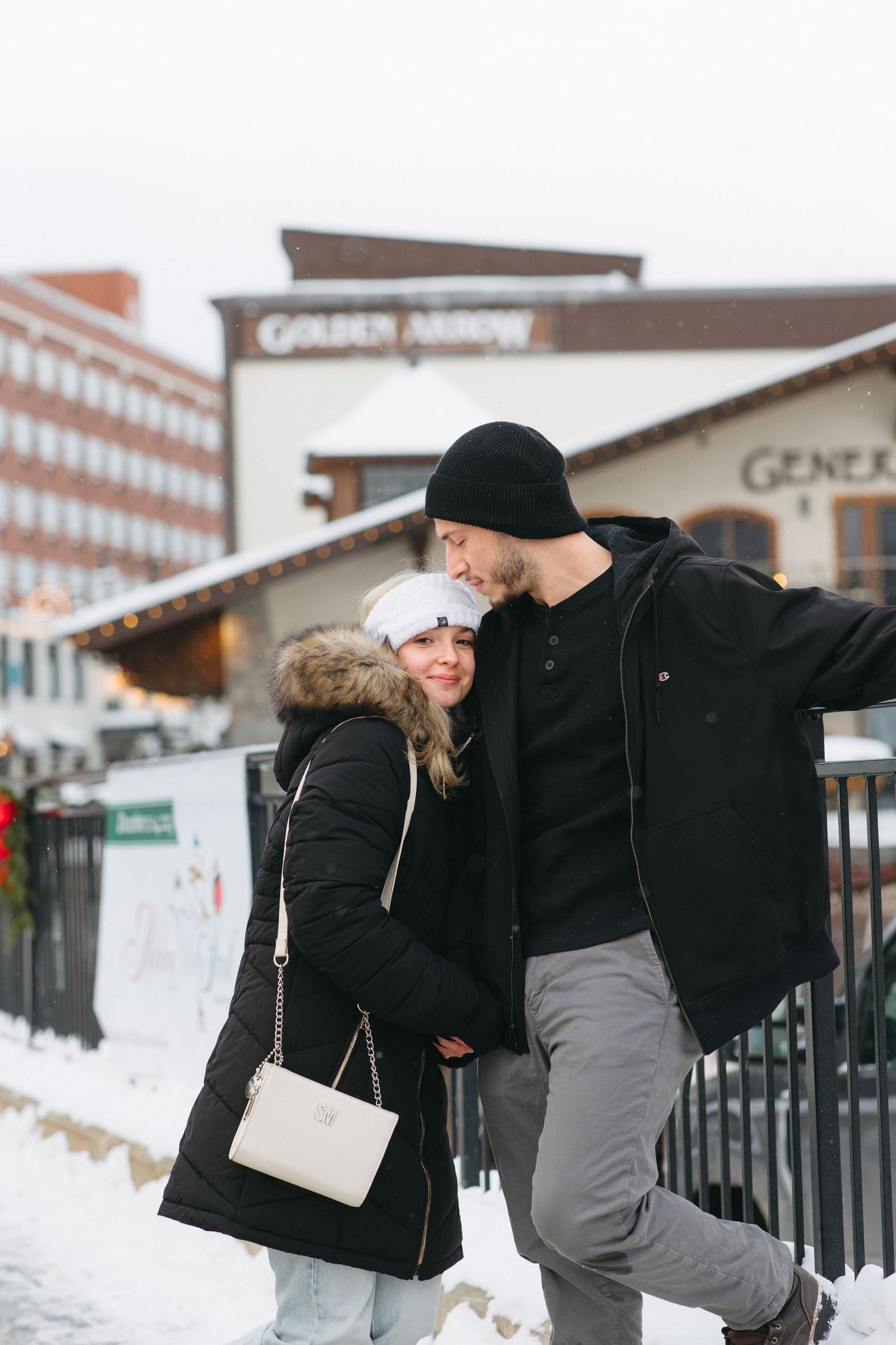 A person in a black winter coat and grey pants performs a dance move in the snowy outdoors.