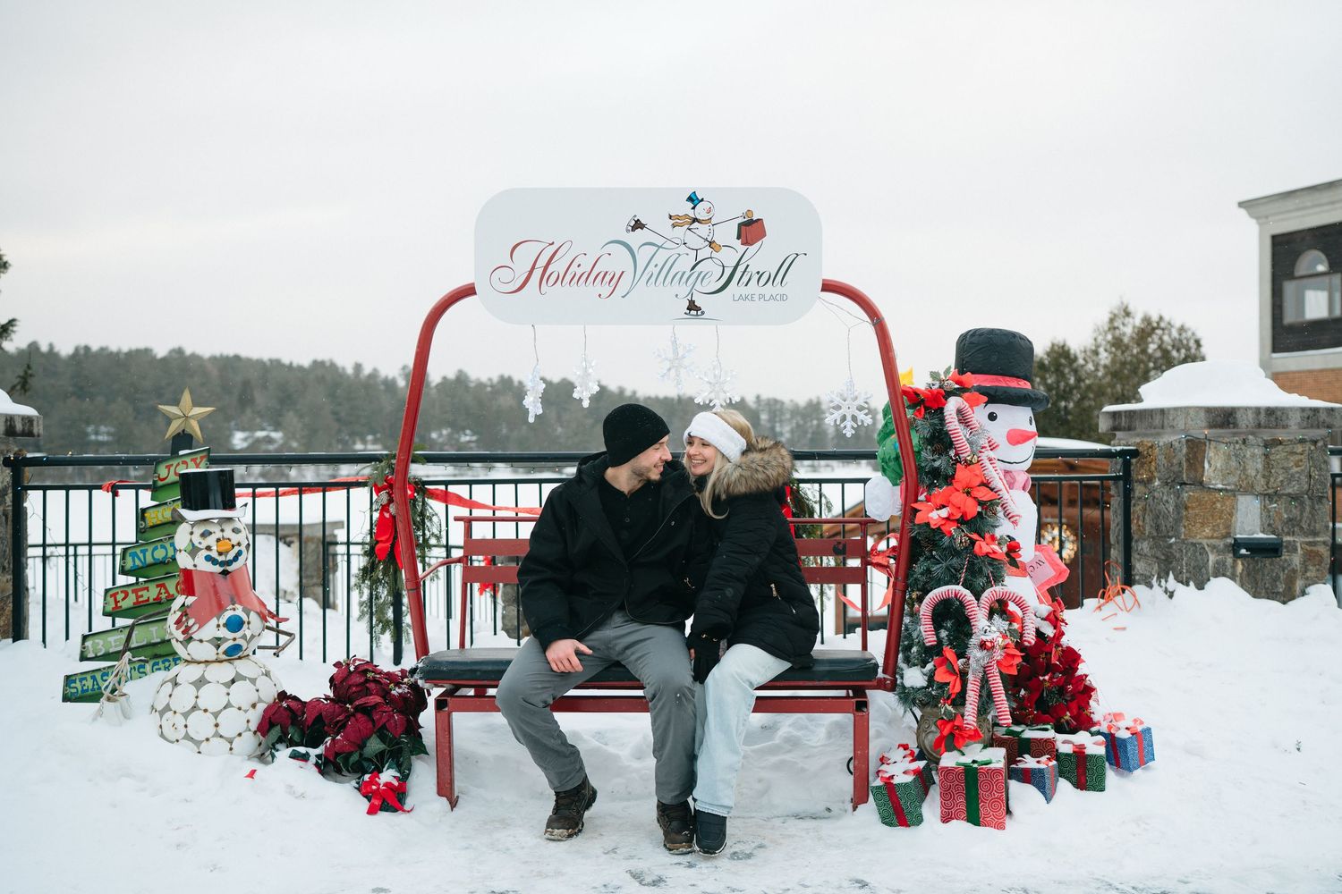 A romantic winter scene with a decorated Christmas arch and gifts in the snow beside a bench.