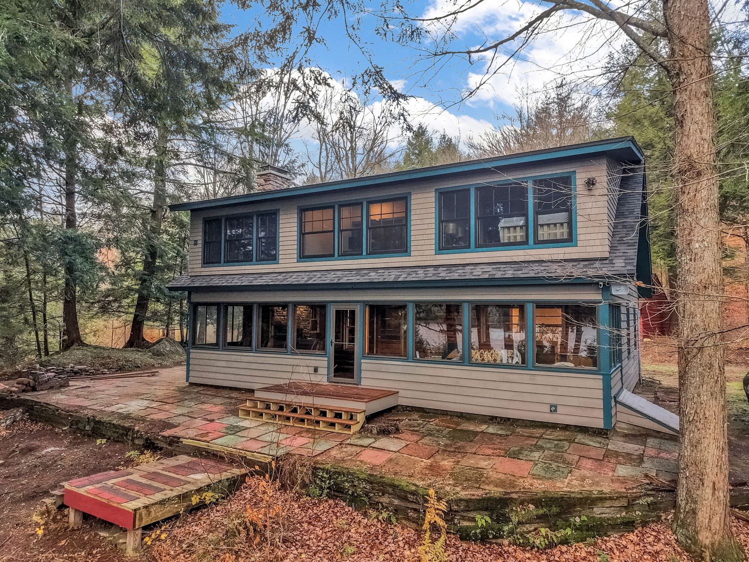 Modern two-story lakeside home with wraparound deck and rustic wooden exterior nestled among pine trees.